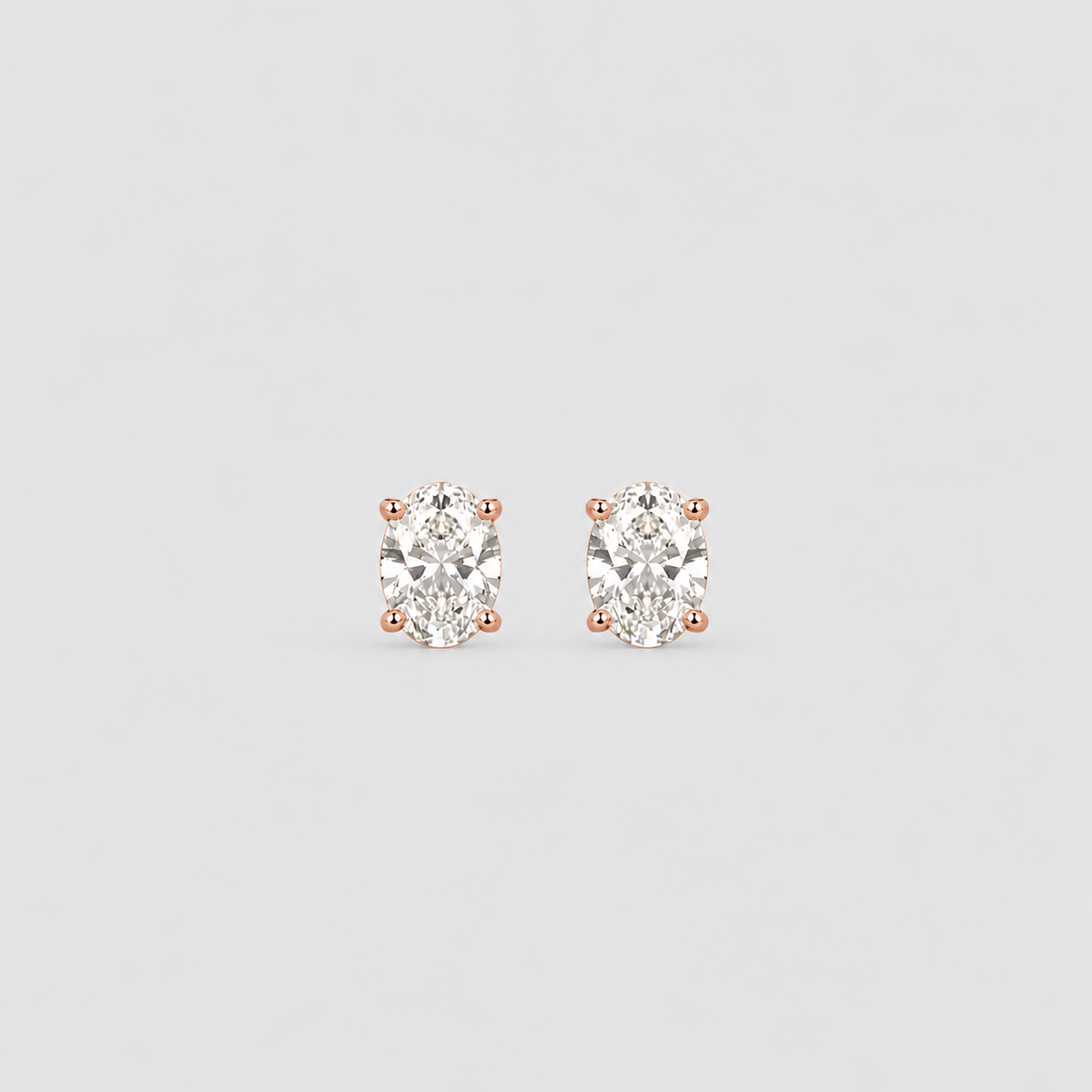 A pair of oval-cut diamond stud earrings in rose gold four-prong settings, shown on a light gray background.