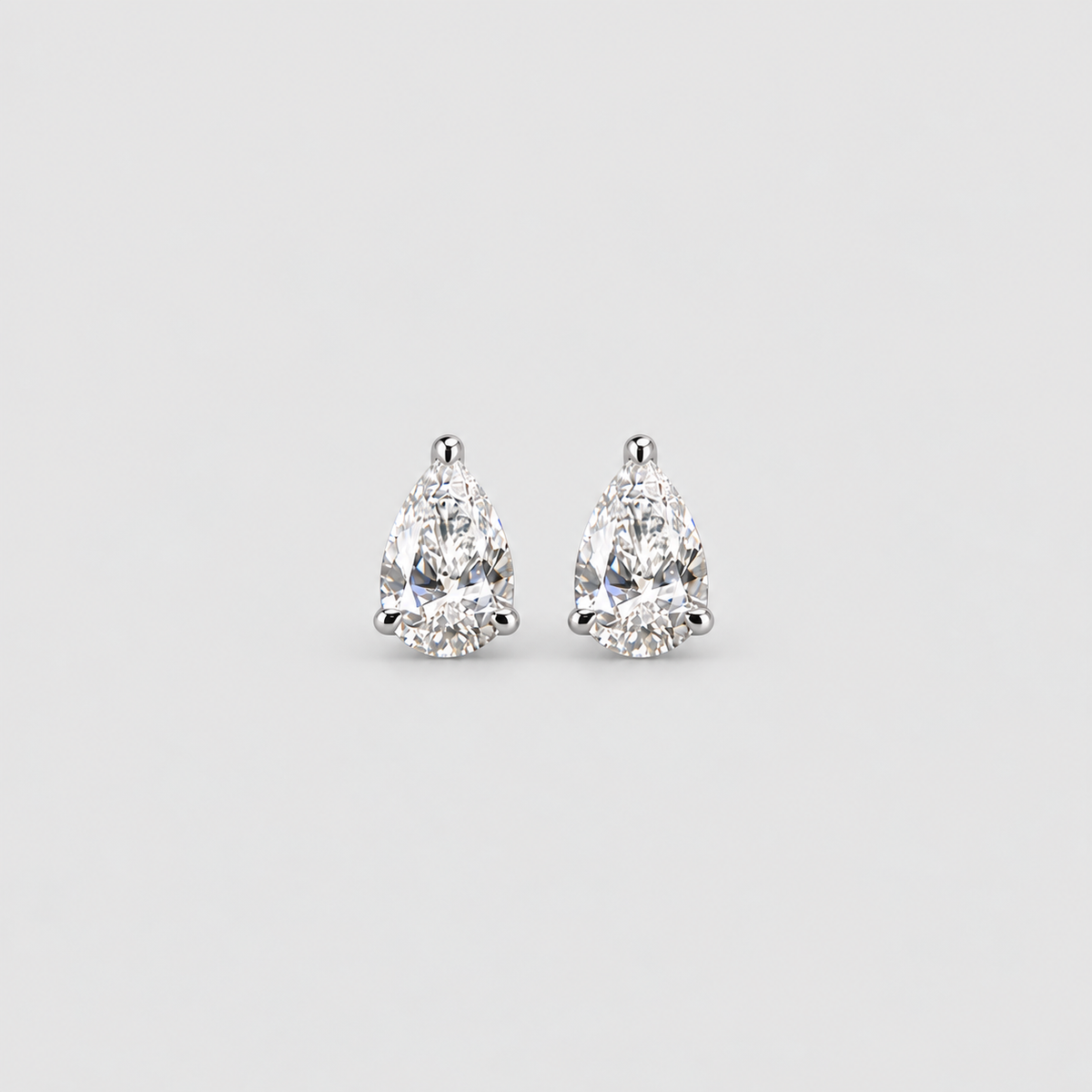 A pair of pear-cut diamond stud earrings in a silver-toned setting, centered on a light gray background.