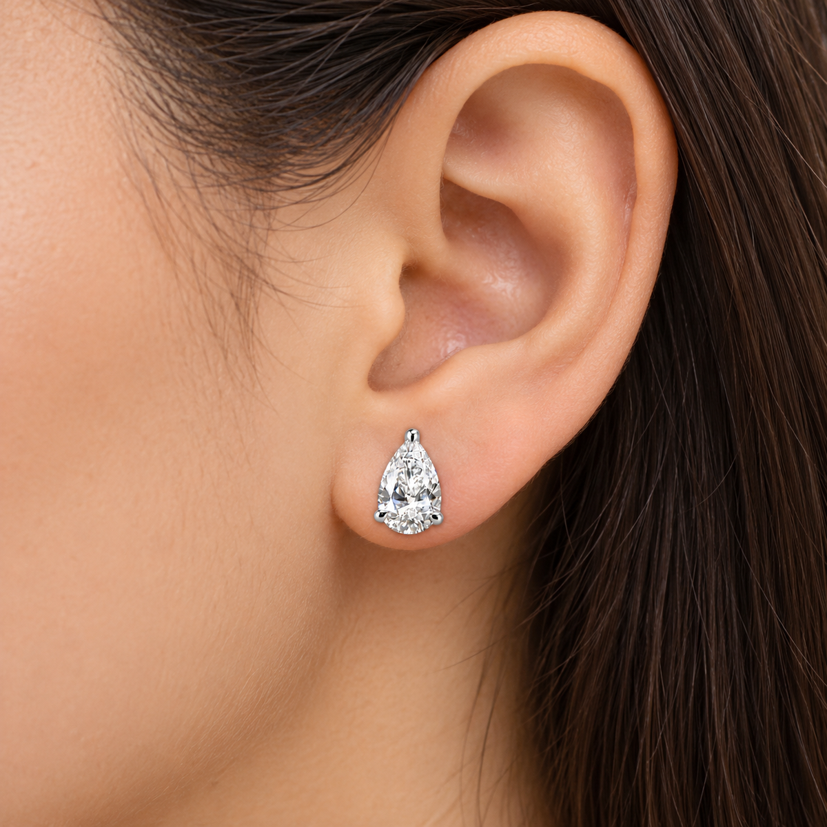 A close-up of a model's ear wearing a single pear-cut diamond stud earring in a silver setting.