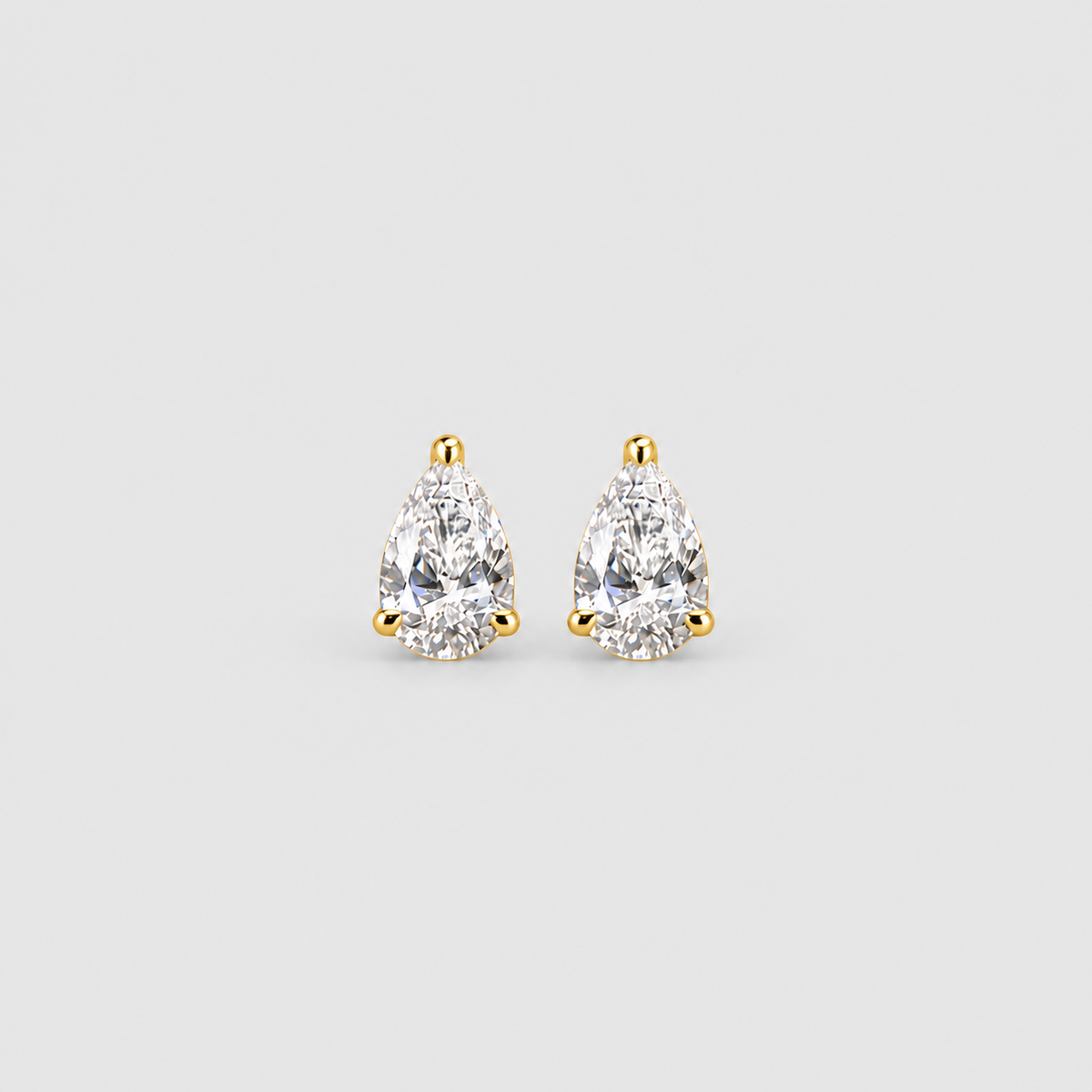 A pair of pear-cut diamond stud earrings in yellow gold settings, shown on a light gray background.