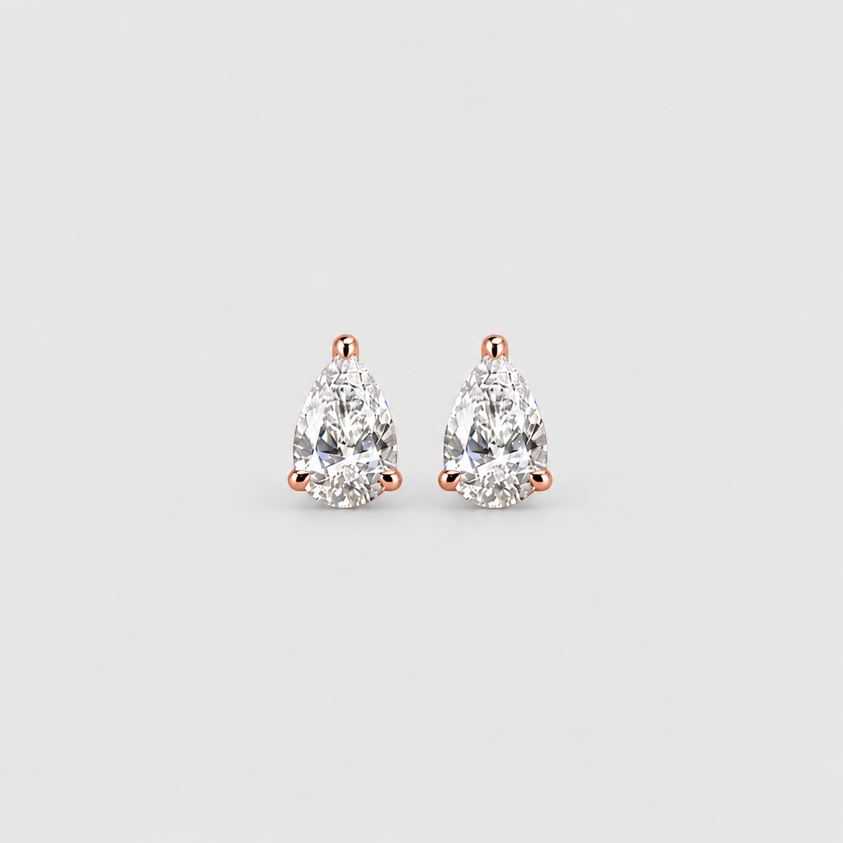 A pair of pear-cut diamond stud earrings in a rose gold setting, photographed on a clean, light gray background.