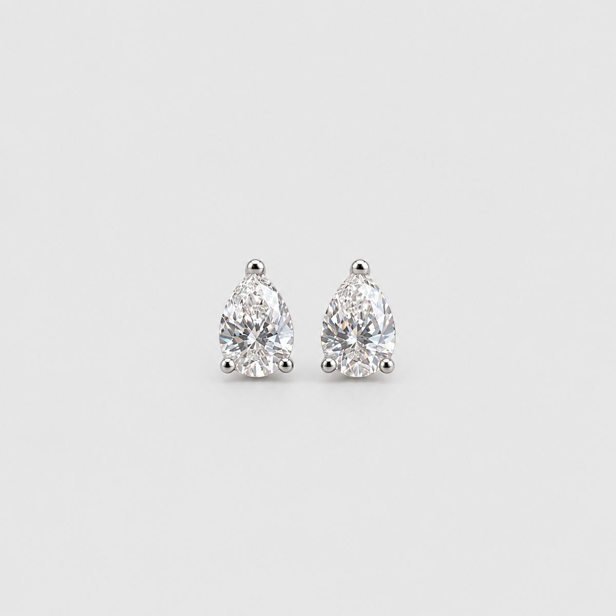 A pair of pear-cut diamond stud earrings in a silver four-prong setting, centered on a light gray background.