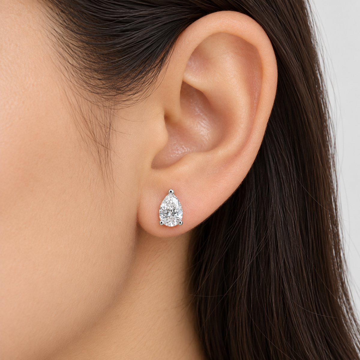 A close-up of a model's ear wearing a single pear-cut diamond stud earring in a silver setting.