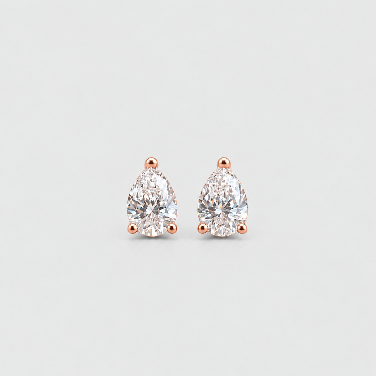 A pair of pear-cut diamond stud earrings in rose gold prong settings, centered on a light gray background.