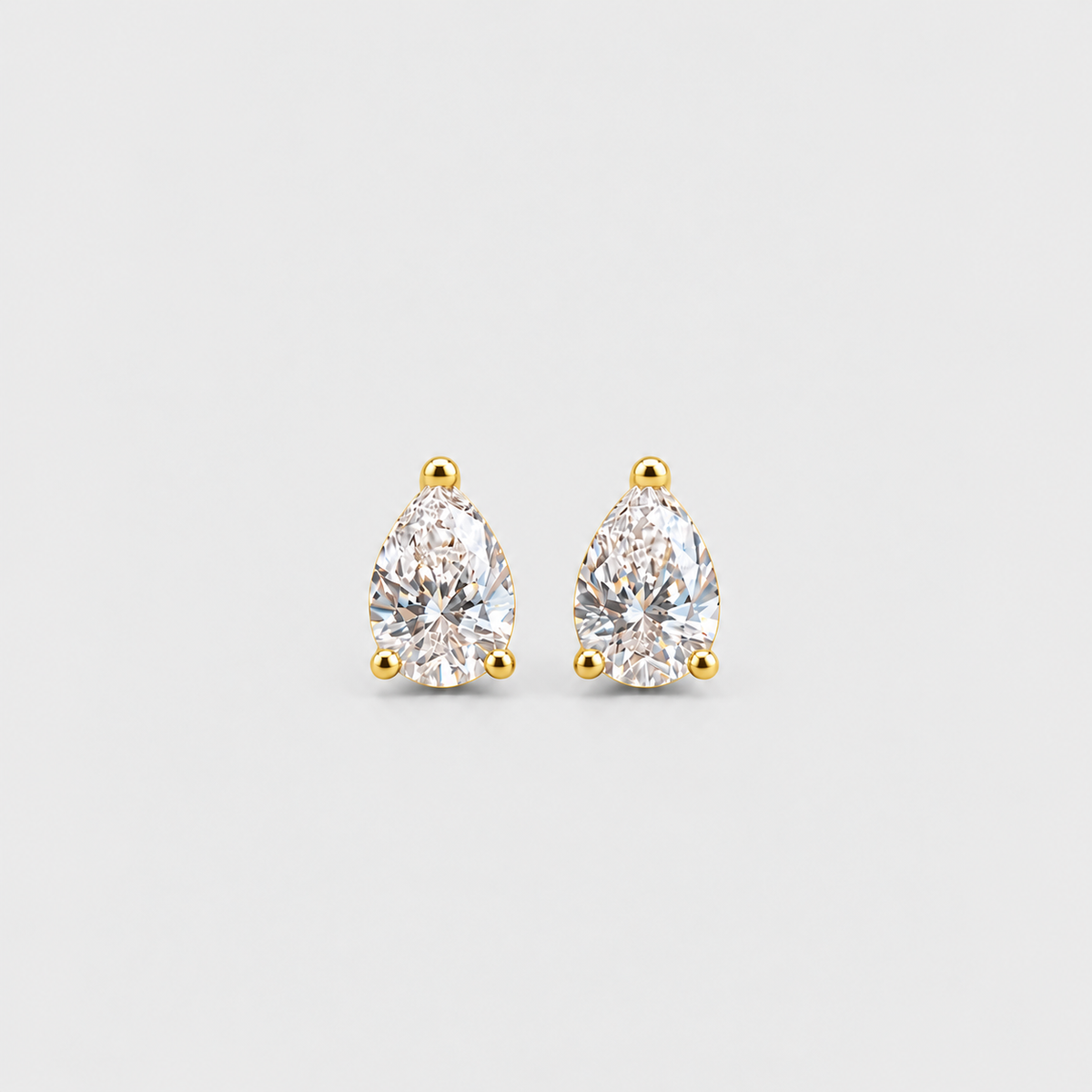 A pair of pear-cut diamond stud earrings in yellow gold prong settings, shown on a light gray background.
