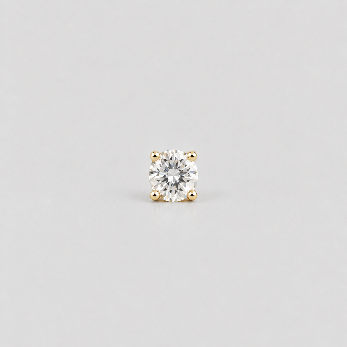 A single round brilliant-cut diamond stud earring in a yellow gold four-prong setting, centered on a light gray background.