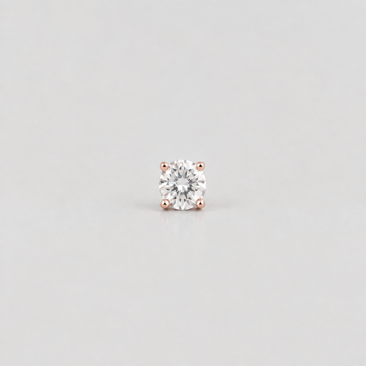 A single round-cut diamond stud earring set in a rose gold four-prong setting, centered on a light gray background.