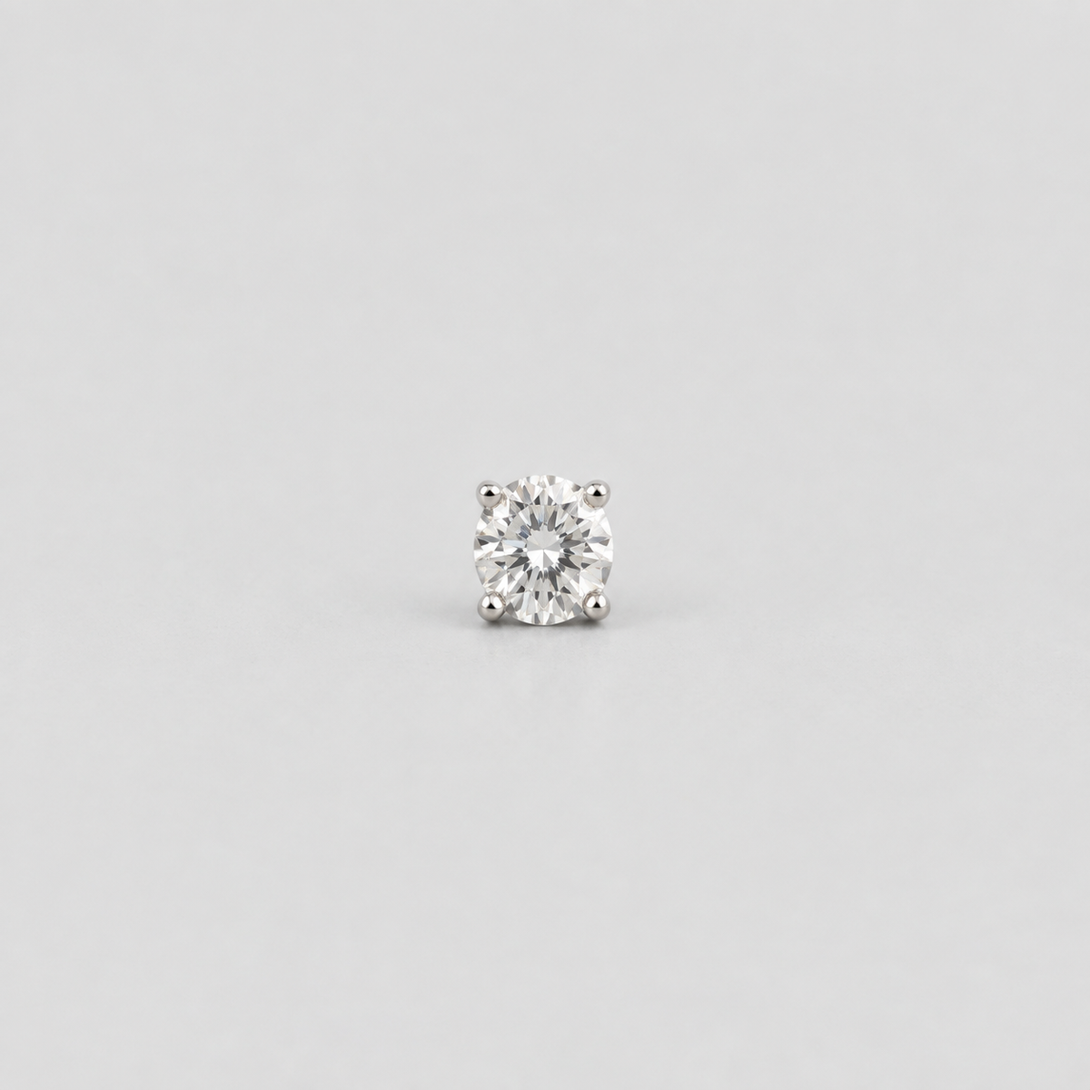 A single round-cut diamond solitaire stud earring in a silver-toned four-prong setting, centered on a light gray background.