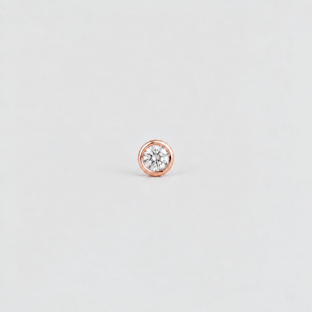 A single round stud earring featuring a clear round-cut gemstone in a polished rose gold bezel setting, centered on a light gray background.