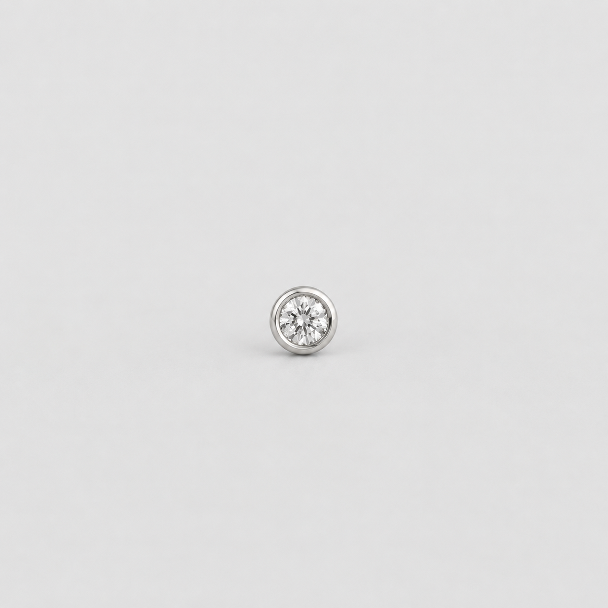 A single round bezel-set diamond stud earring in a silver-toned metal, centered on a light gray background.