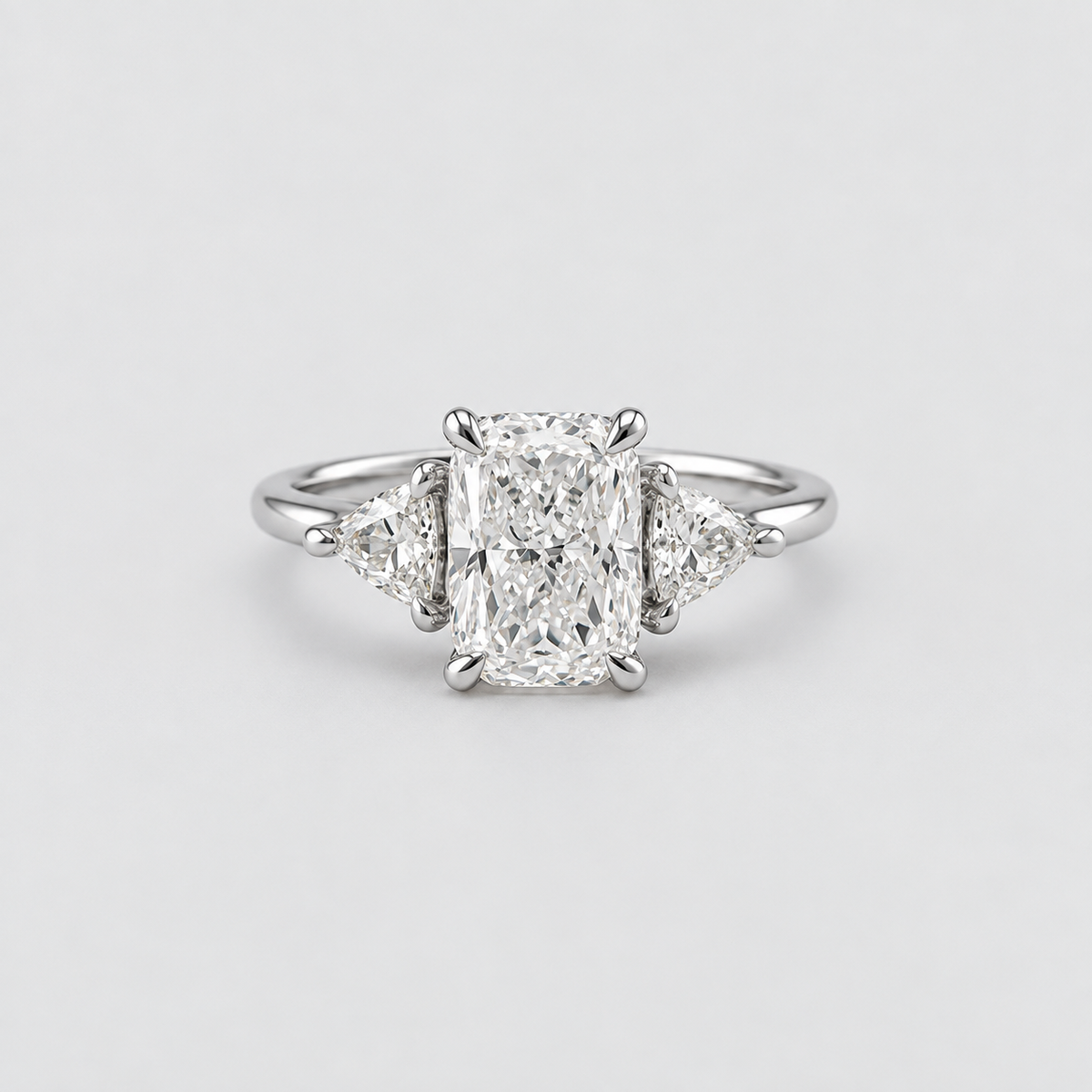 An elegant diamond ring featuring a central rectangular radiant-cut diamond flanked by two small triangular diamonds on a polished silver-colored band, set against a clean light gray background.