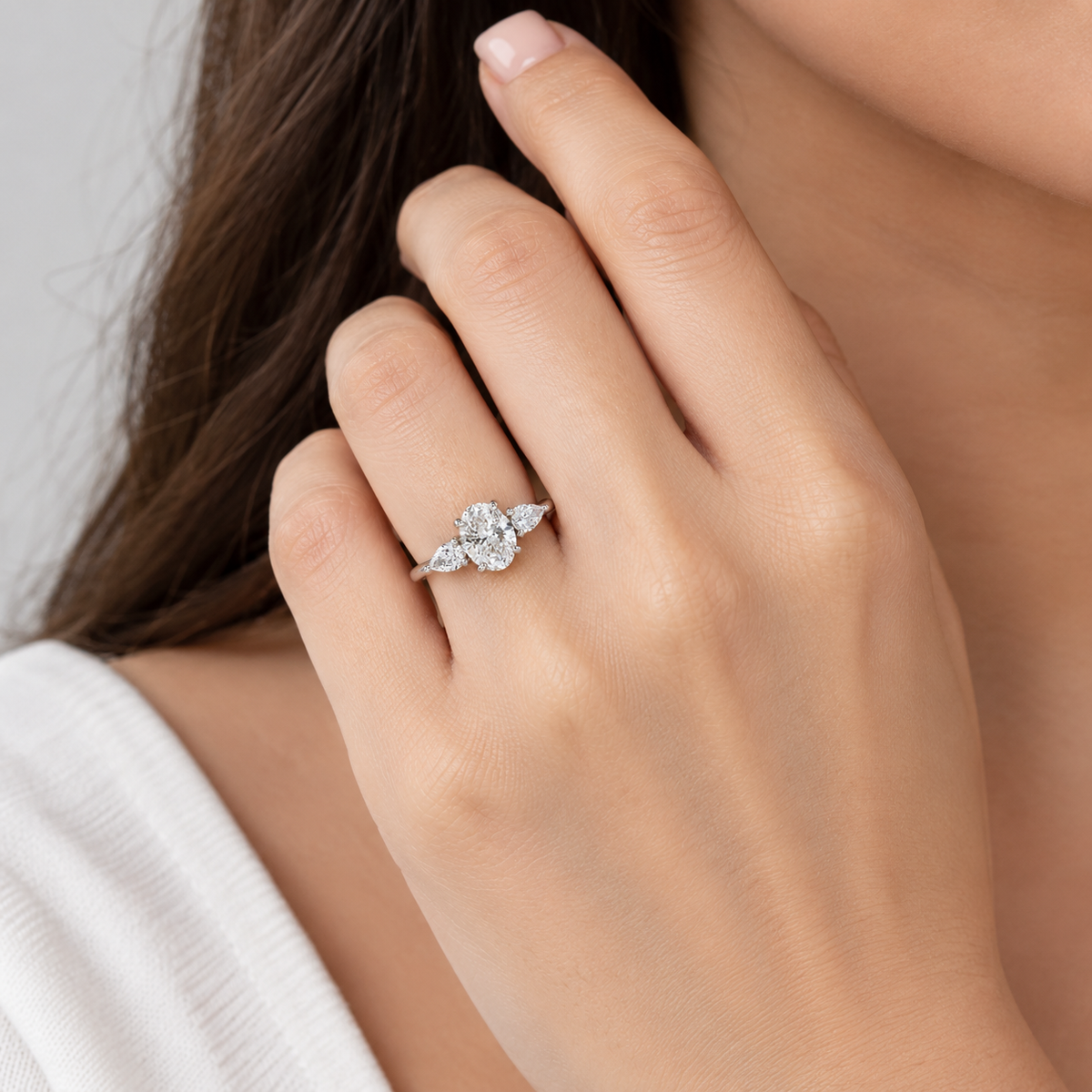 A close-up of a woman's hand wearing a silver-toned diamond ring with a central round diamond and smaller side diamonds, set against her neck and hair.