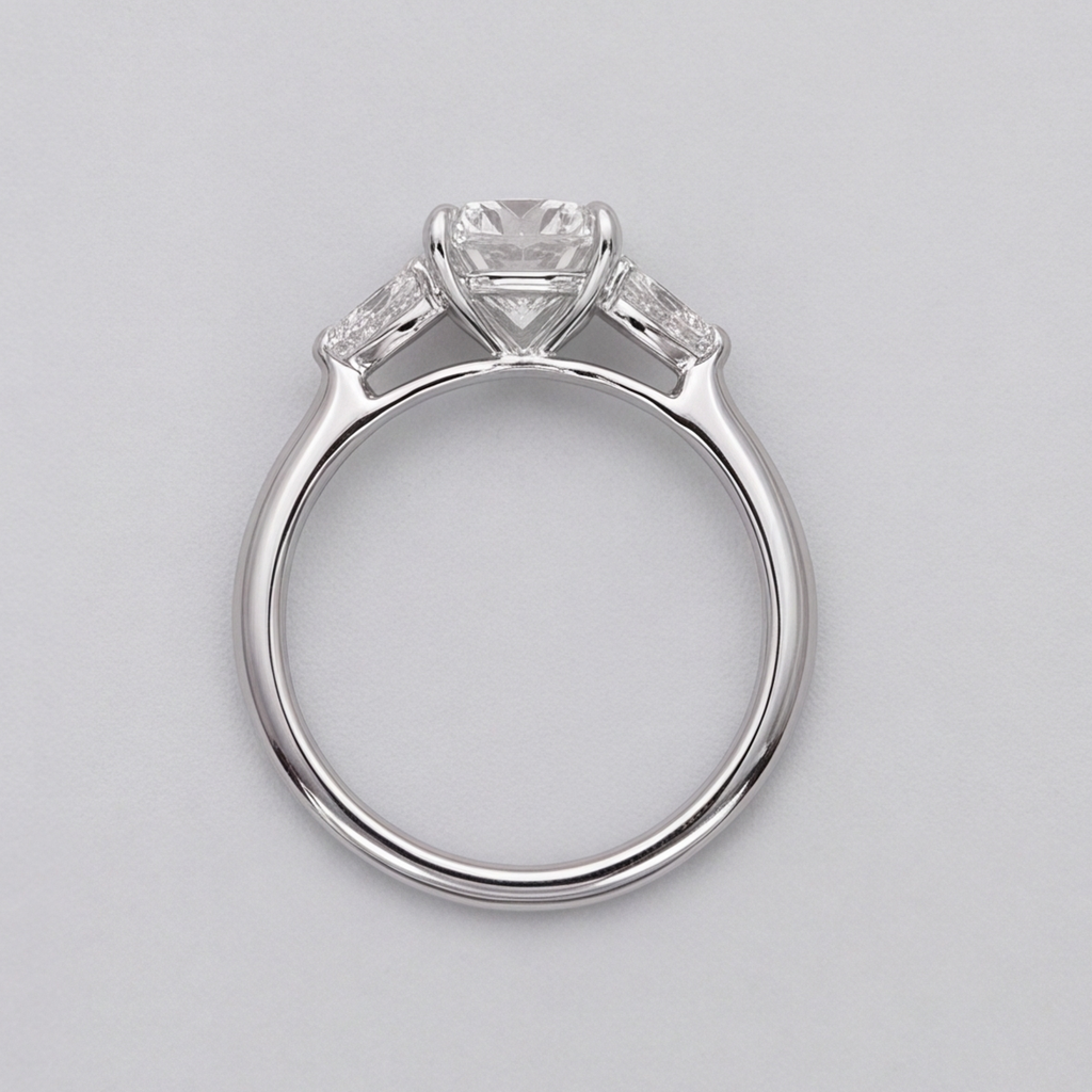 A silver-tone solitaire engagement ring with a round center stone and small side stones, shown from a top-down view on a light gray background.