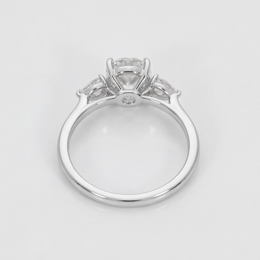 A silver-toned diamond ring with a large round center stone and smaller side stones, shown from a top-down view on a light gray background.