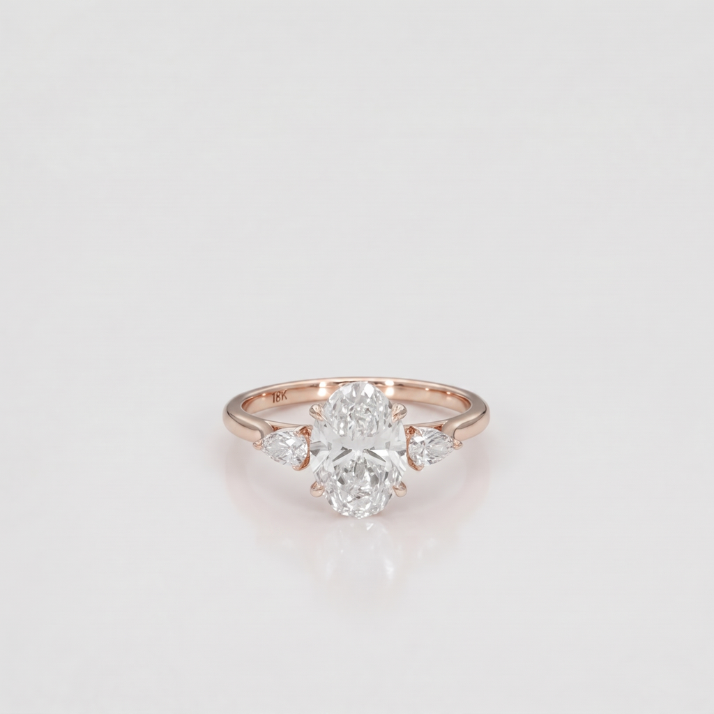A rose gold diamond ring with a central oval-cut diamond flanked by two smaller round-cut diamonds on the shoulders, set against a clean white background.