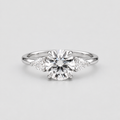 A silver engagement ring featuring a round brilliant-cut center stone with two small round side stones and two marquise-cut side stones, set on a plain light gray background.