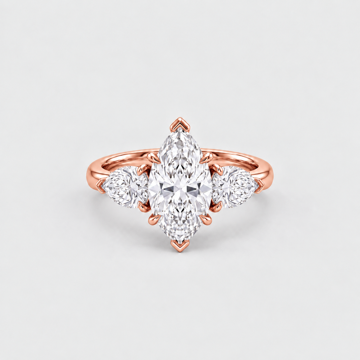 A rose gold ring featuring a marquise-cut center diamond flanked by two round diamonds on a clean, light gray background.