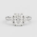 A radiant cut diamond engagement ring with triangular side diamonds on a polished silver-colored band, shown against a light gray background.