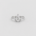 A silver diamond ring with a pear-cut center stone and smaller marquise-cut side stones, shown on a light gray background.