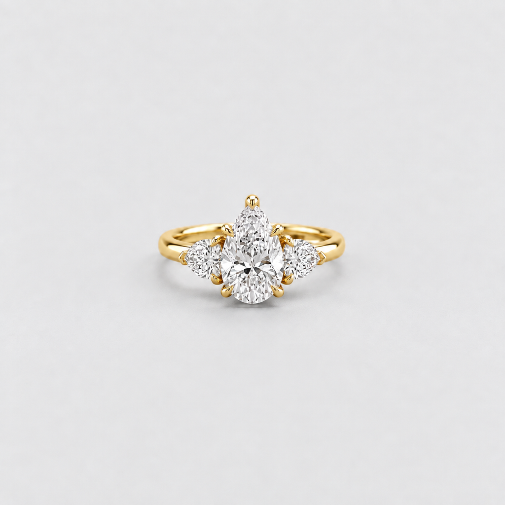 A yellow gold ring featuring a pear-cut center diamond surrounded by three smaller round diamonds, set on a plain light gray background.