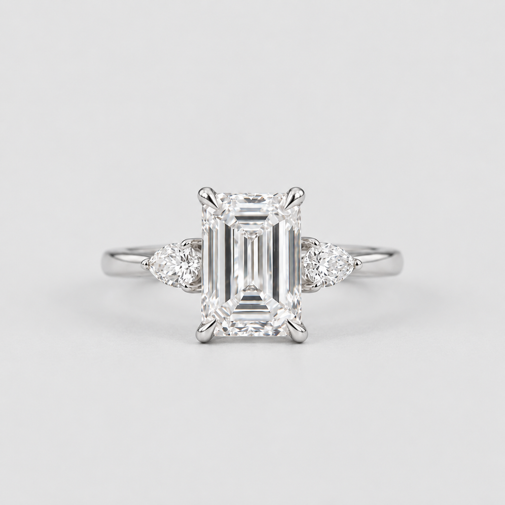 An emerald-cut diamond engagement ring with a silver-toned band and small round diamonds on either side, centered on a light gray background.