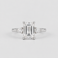 An emerald-cut diamond engagement ring with a silver-toned band and small round diamonds on either side, centered on a light gray background.