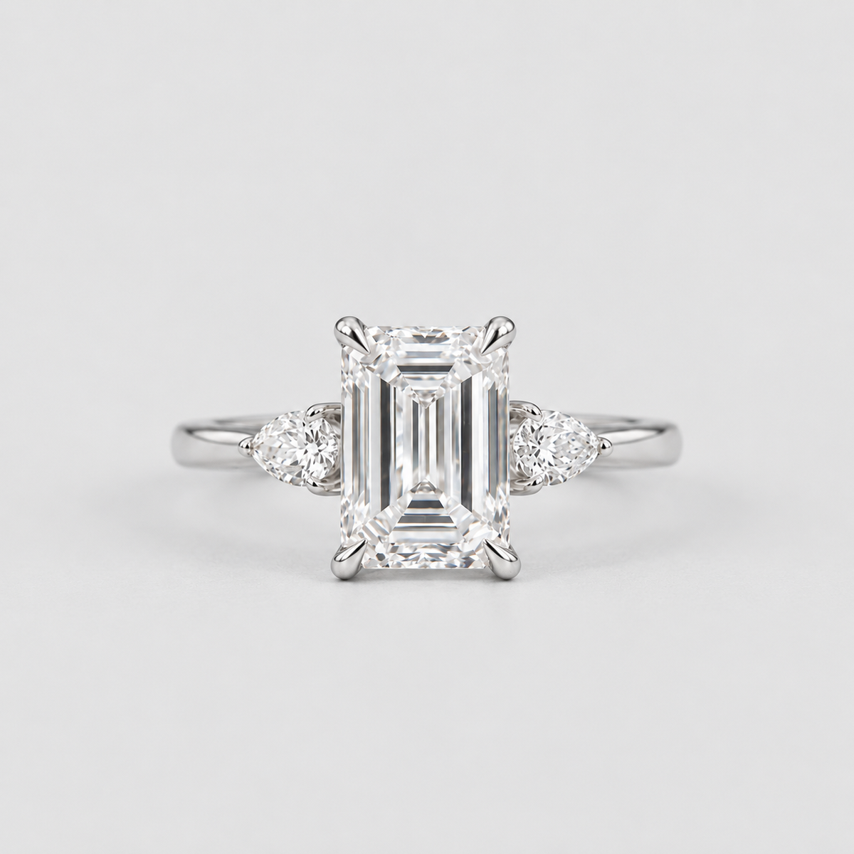 An emerald-cut diamond engagement ring with a silver-toned band and small round diamonds on either side, centered on a light gray background.