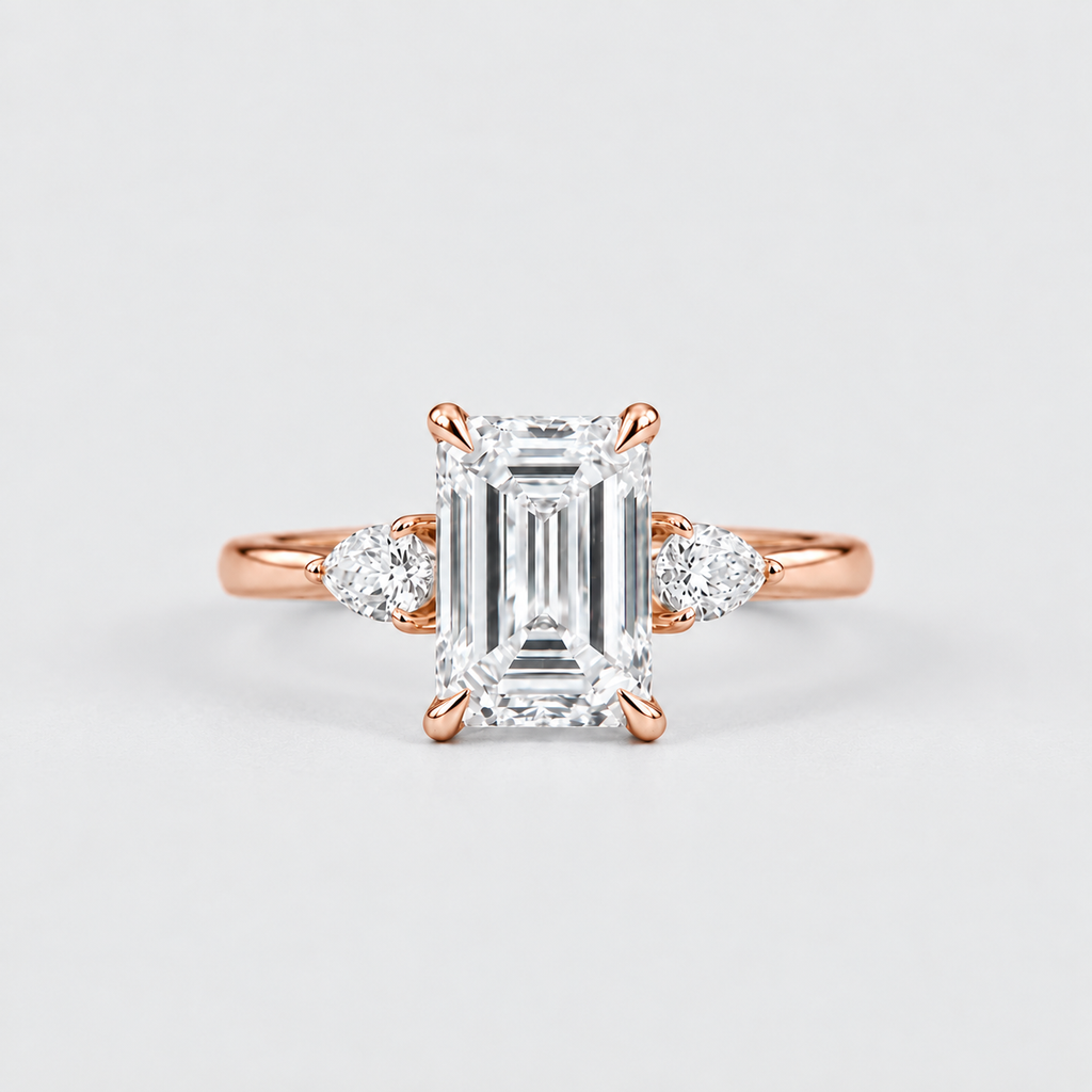 An emerald-cut diamond engagement ring in rose gold with small round diamonds on either side of the band, set against a clean light gray background.