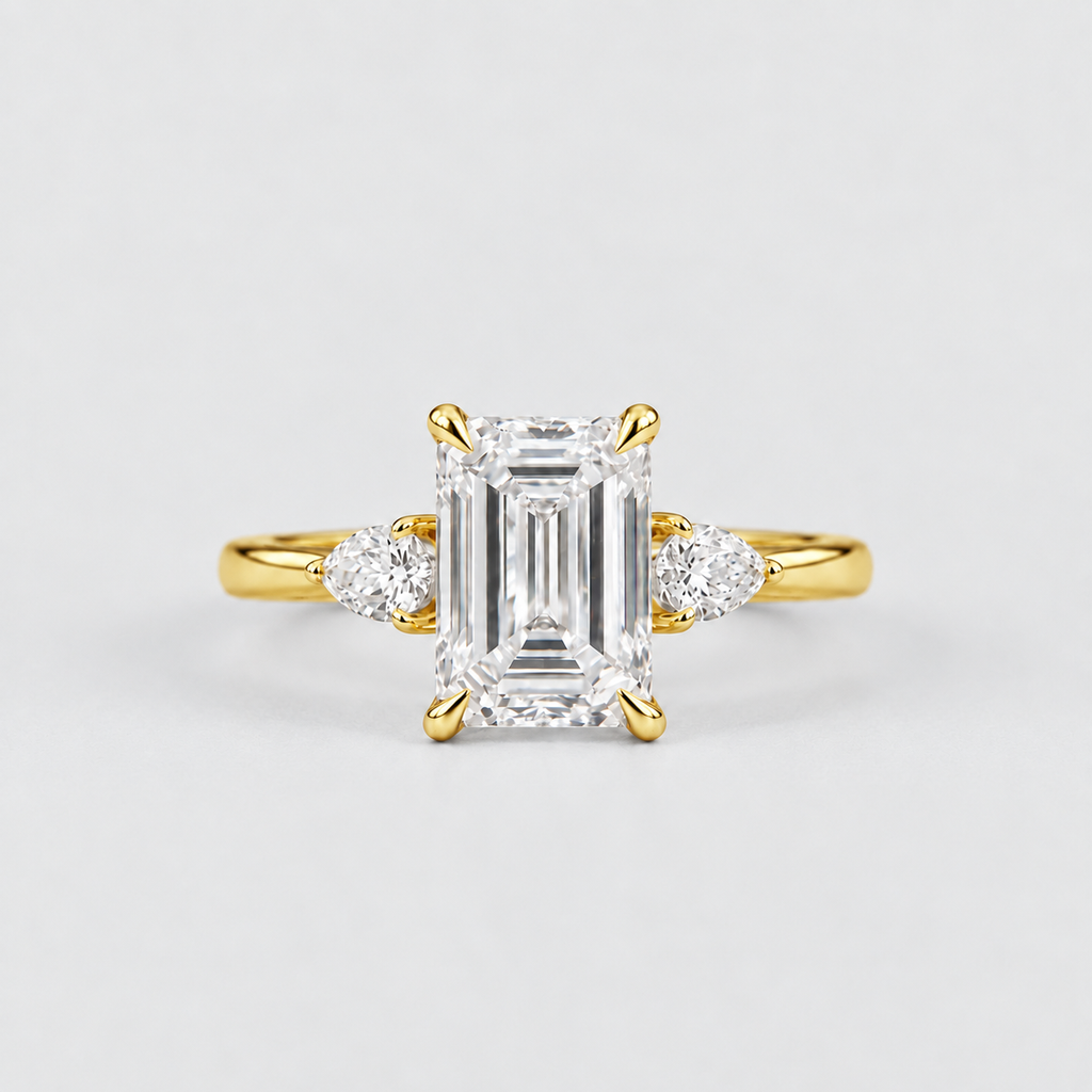 A yellow gold engagement ring featuring a large emerald-cut diamond center stone and two smaller round diamonds on either side of the band, set against a clean light gray background.
