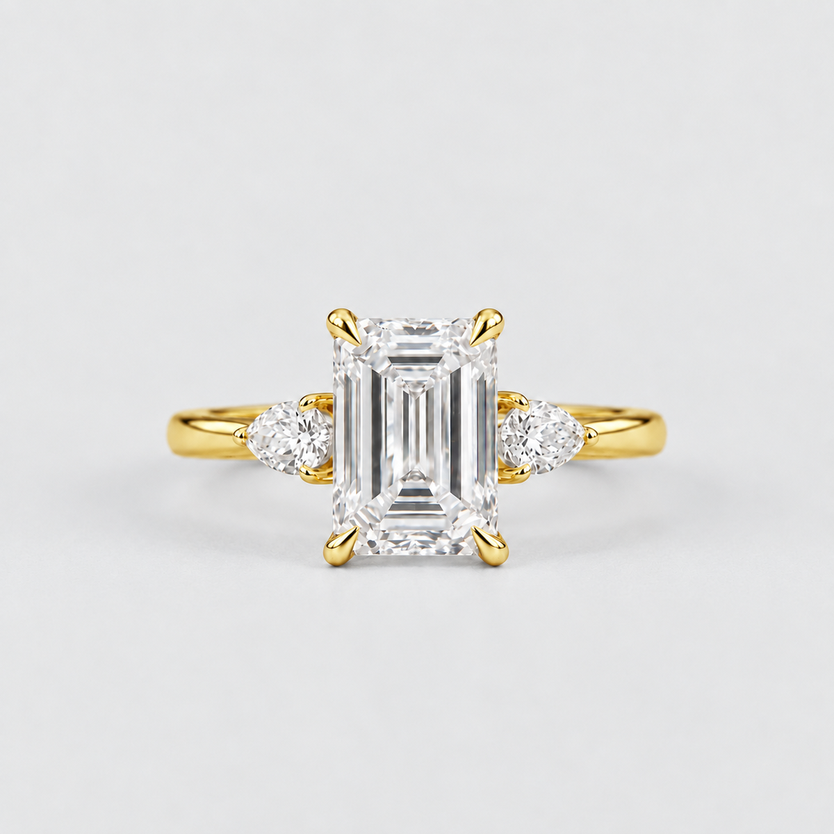 A yellow gold engagement ring featuring a large emerald-cut diamond center stone and two smaller round diamonds on either side of the band, set against a clean light gray background.