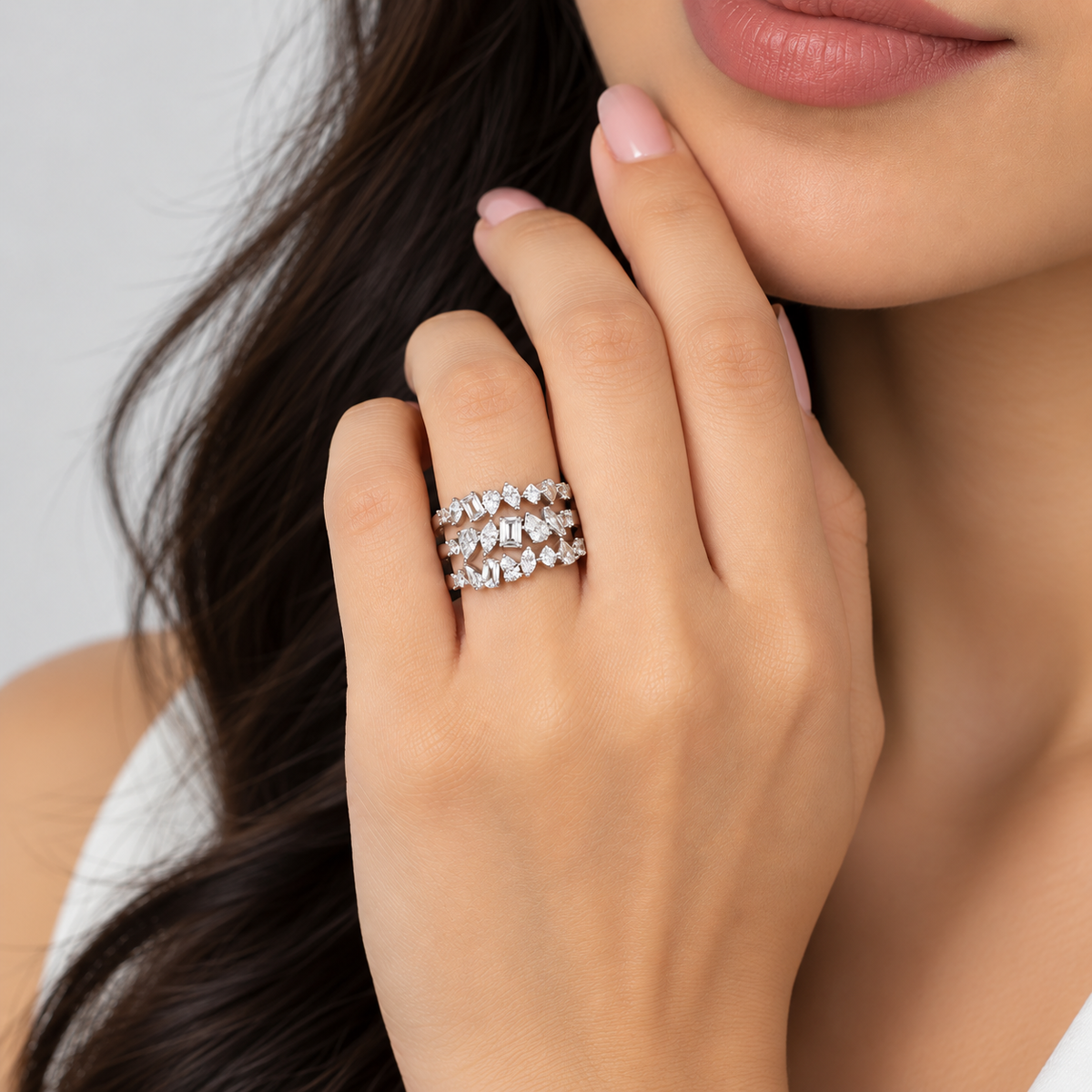 A close-up lifestyle shot of a woman's hand wearing three stacked silver rings set with clear marquise-cut gemstones. The background is a soft, neutral light gray.