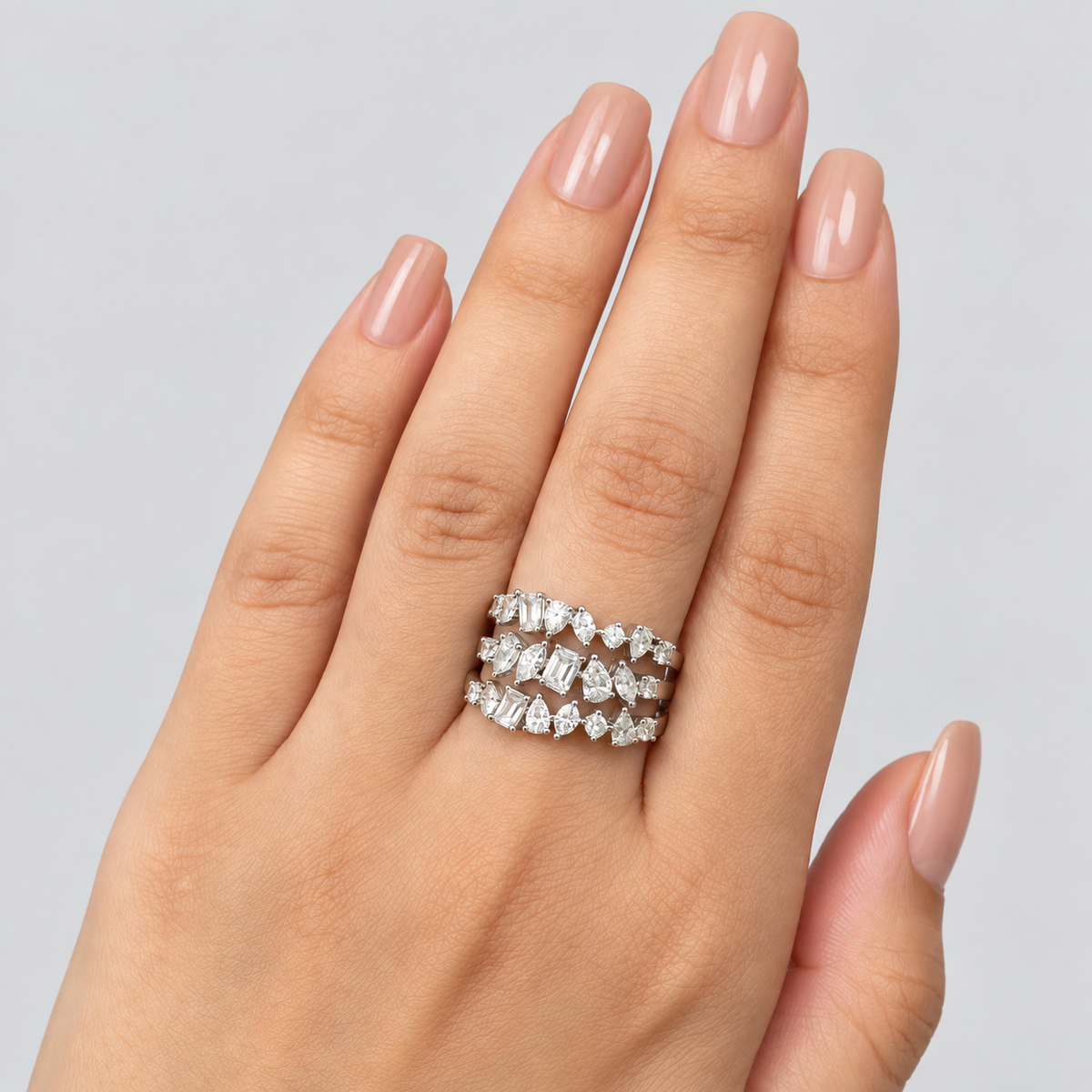 A close-up of a hand wearing three stacked silver rings set with clear baguette-cut gemstones, shown against a light gray background.