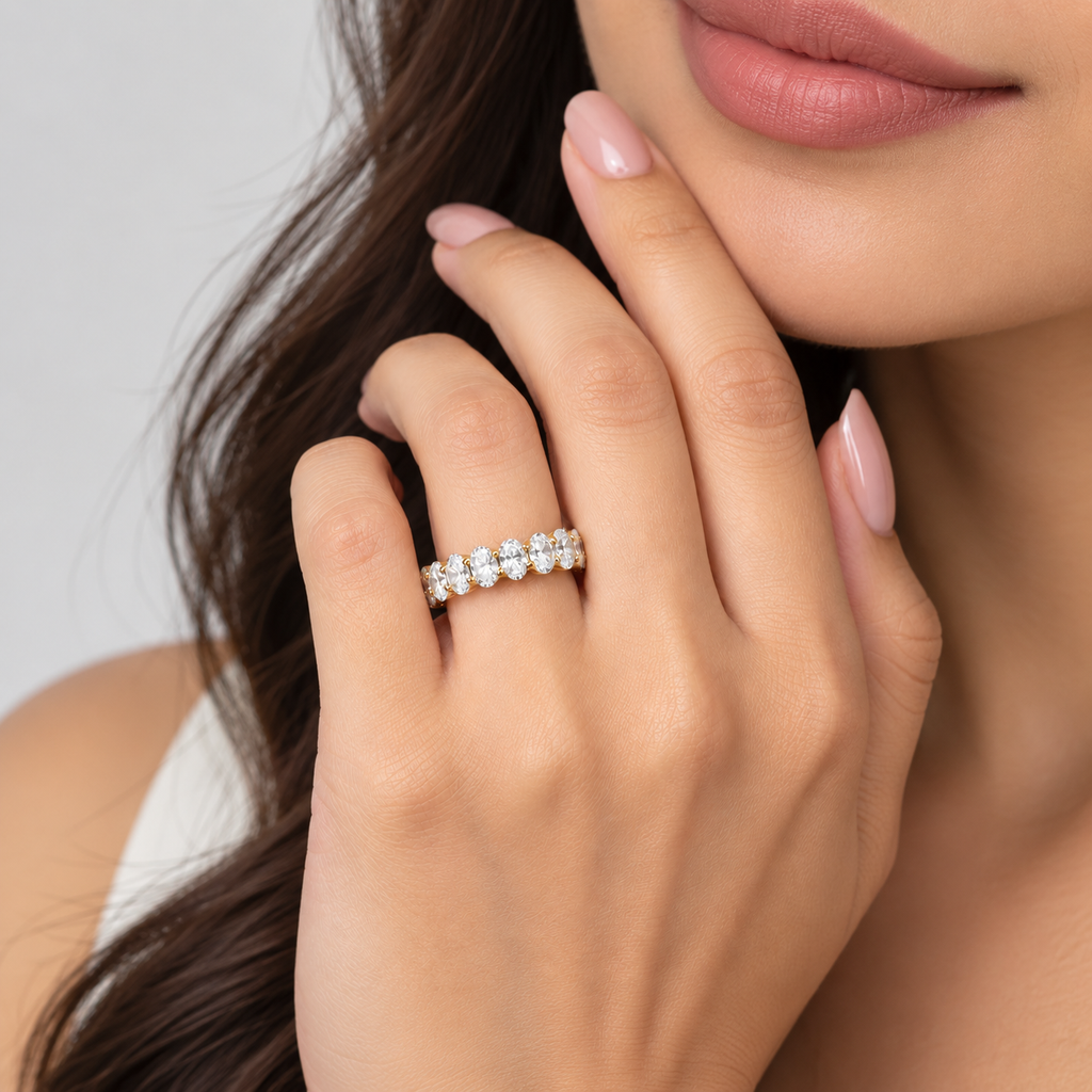 A close-up lifestyle shot of a woman's hand wearing a five-stone diamond ring on a silver band, with her face and hair softly blurred in the background.