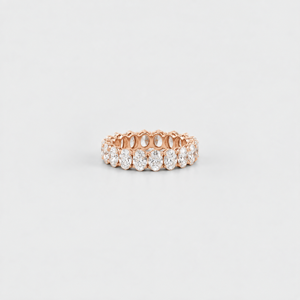 A rose gold eternity ring featuring a row of round-cut clear gemstones, photographed on a clean, light gray background.