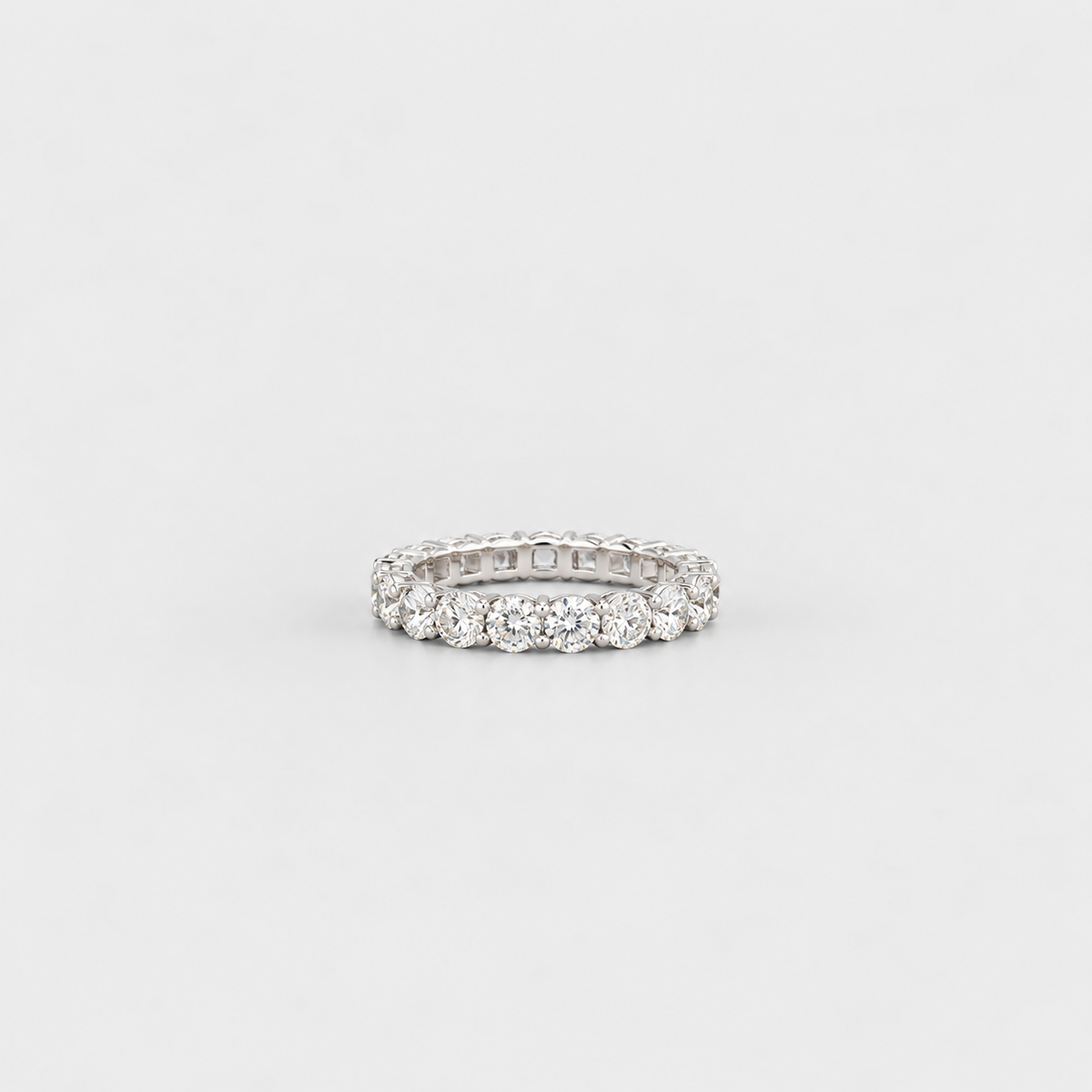 A silver-tone eternity ring set with round brilliant-cut diamonds, photographed on a seamless light gray background.