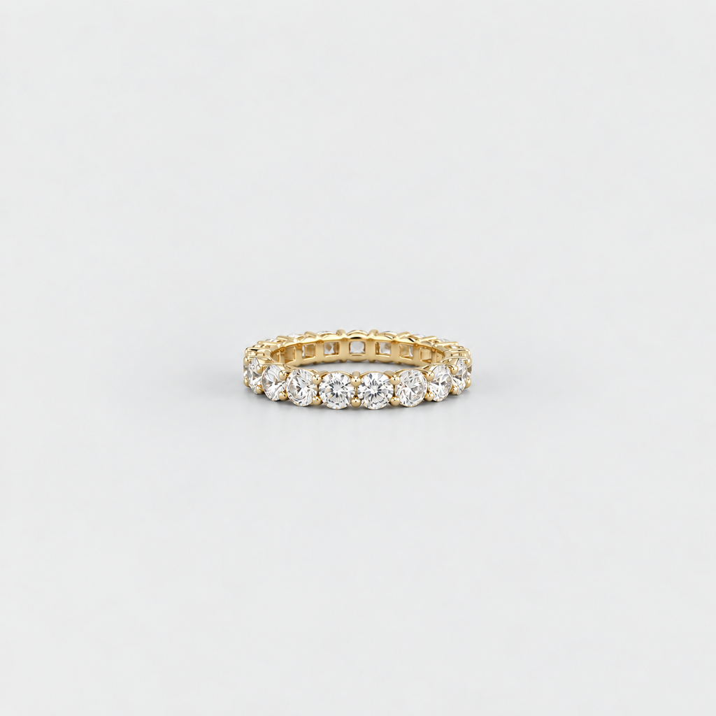 A yellow gold eternity ring set with round brilliant-cut diamonds, photographed on a clean, light gray background.
