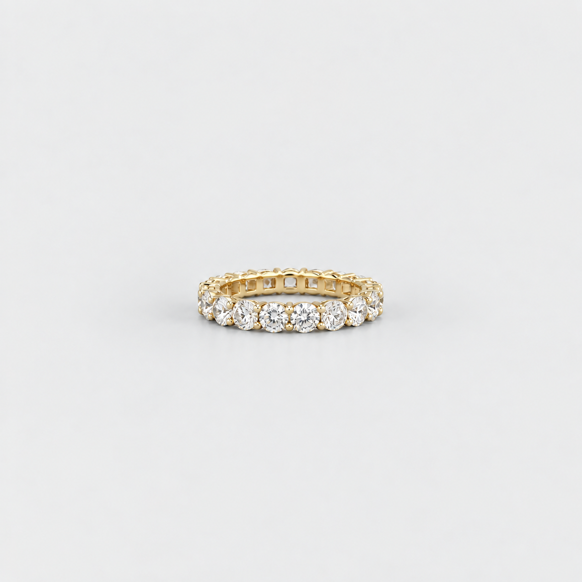 A yellow gold eternity ring set with round brilliant-cut diamonds, photographed on a clean, light gray background.