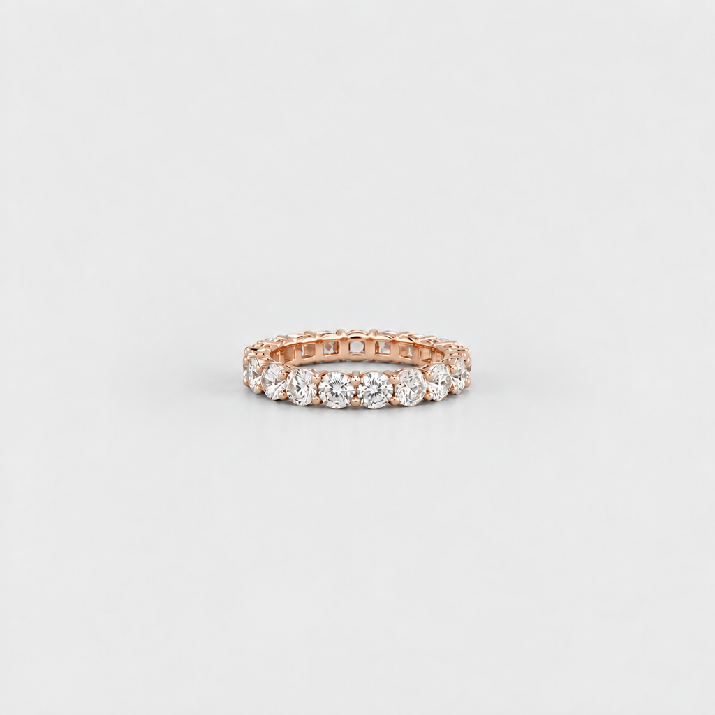 A rose gold eternity ring featuring a row of round-cut clear gemstones, photographed on a clean, light gray background.