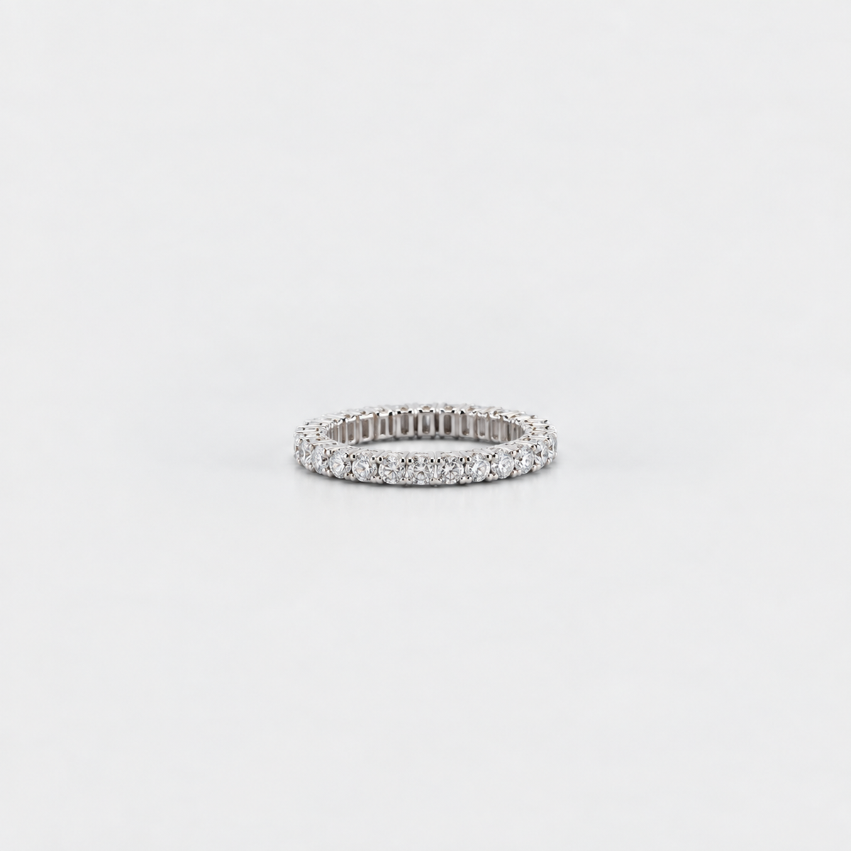 A slim silver eternity ring paved with small round-cut clear stones, centered on a seamless light gray background.