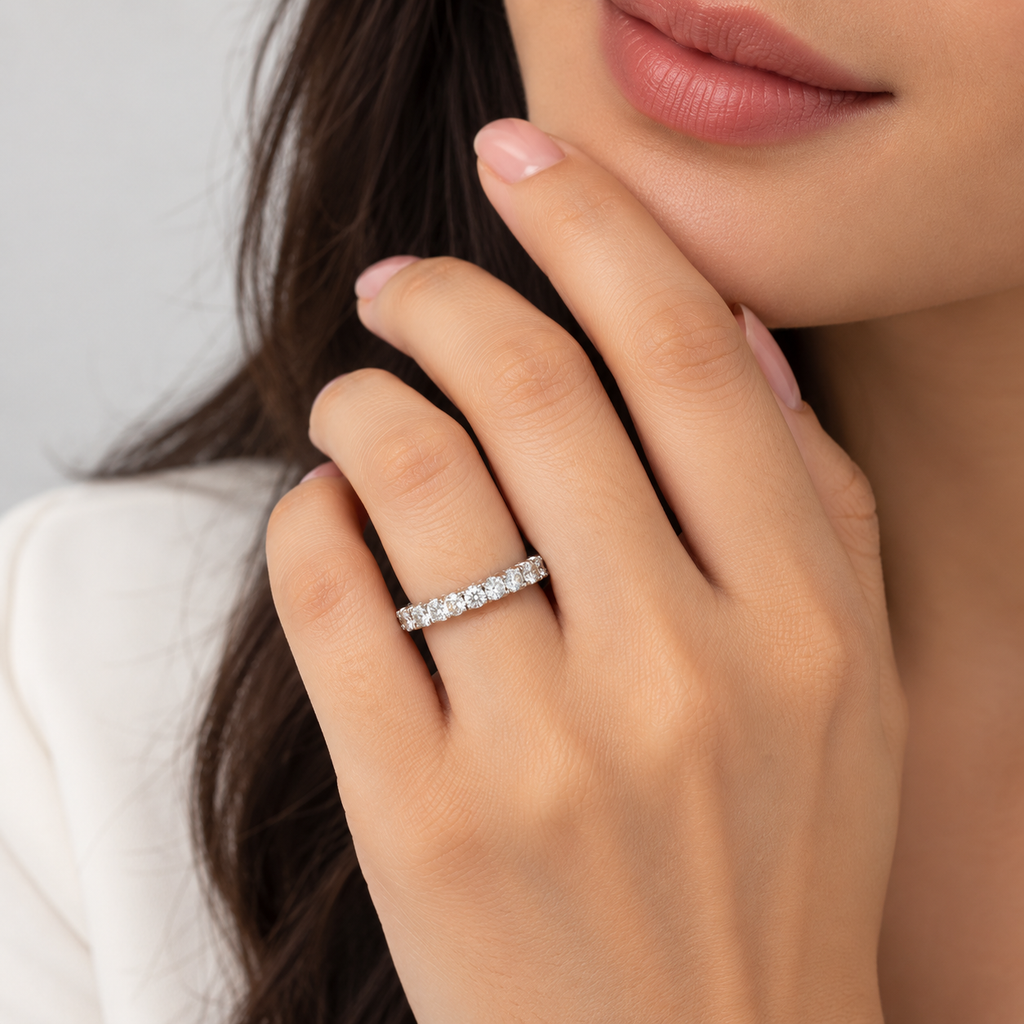 A close-up lifestyle shot of a woman wearing a silver eternity ring set with clear stones on her finger. The ring is shown on her hand, with her lips, hand, and dark hair visible against a soft, light gray background.