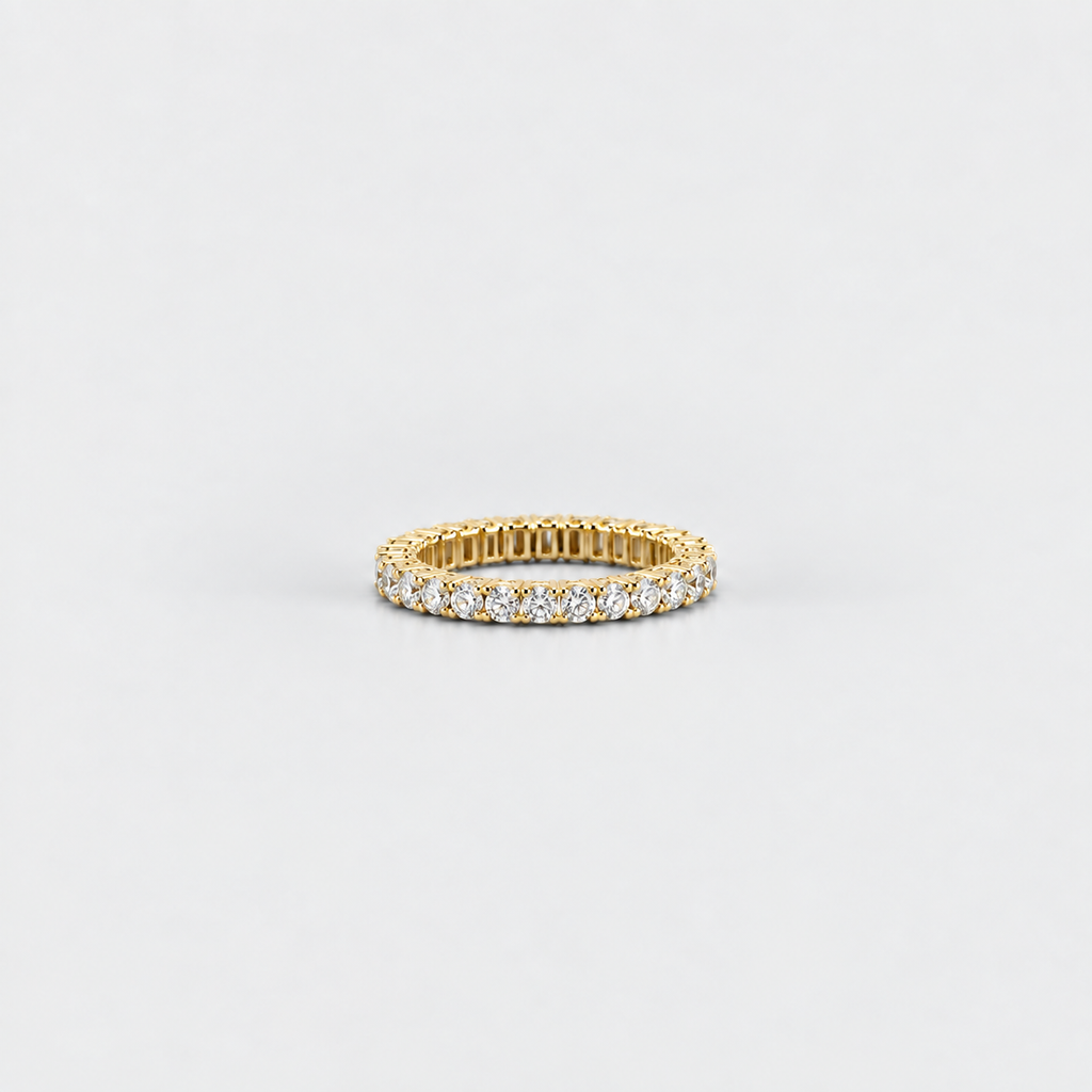 A yellow gold eternity ring set with round brilliant-cut diamonds, photographed on a clean, light gray background.
