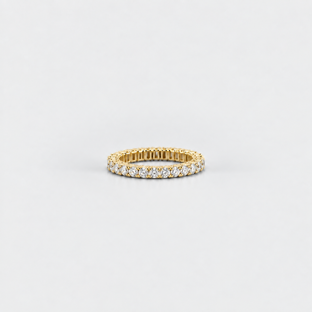 A yellow gold eternity ring set with round brilliant-cut diamonds, photographed on a clean, light gray background.