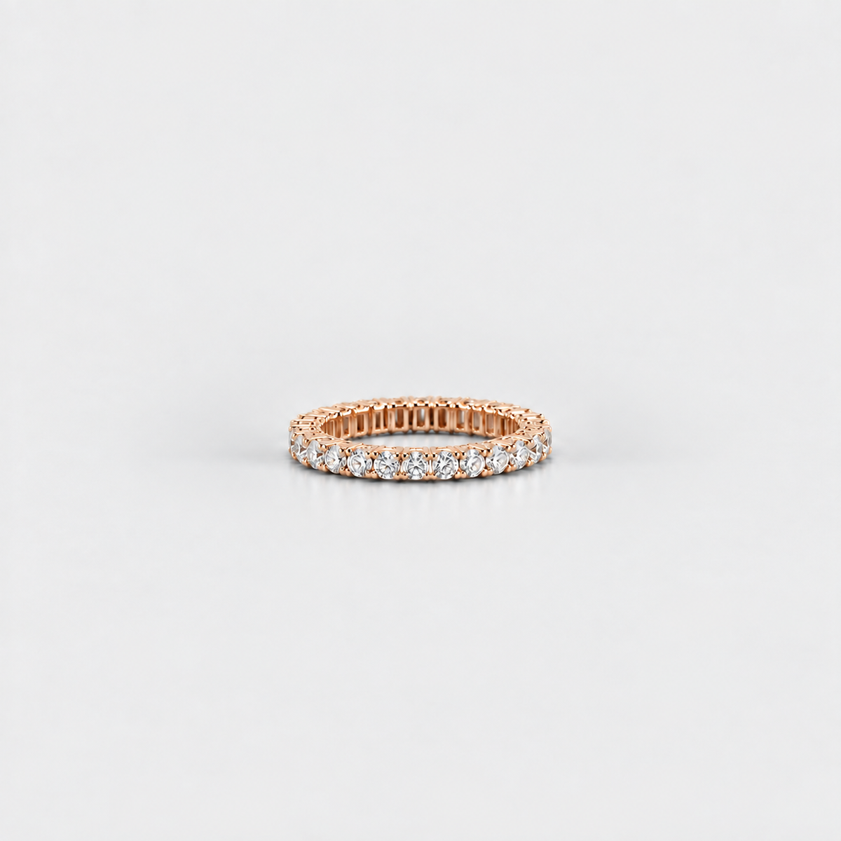 A rose gold eternity ring set with round brilliant-cut diamonds, photographed on a clean, light gray background.
