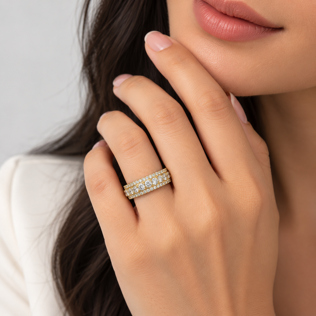 A close-up lifestyle shot of a woman wearing a gold double-row diamond eternity band ring on her hand.