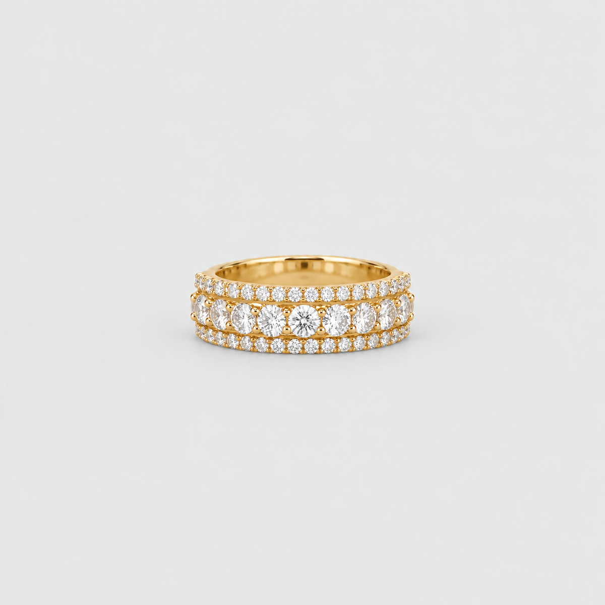 A yellow gold eternity ring featuring three rows of round brilliant-cut and cushion-cut diamonds, photographed on a clean, light gray background.