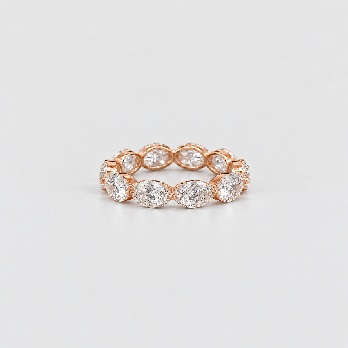 A rose gold eternity ring featuring a row of marquise-cut diamonds, photographed on a clean, light gray background.
