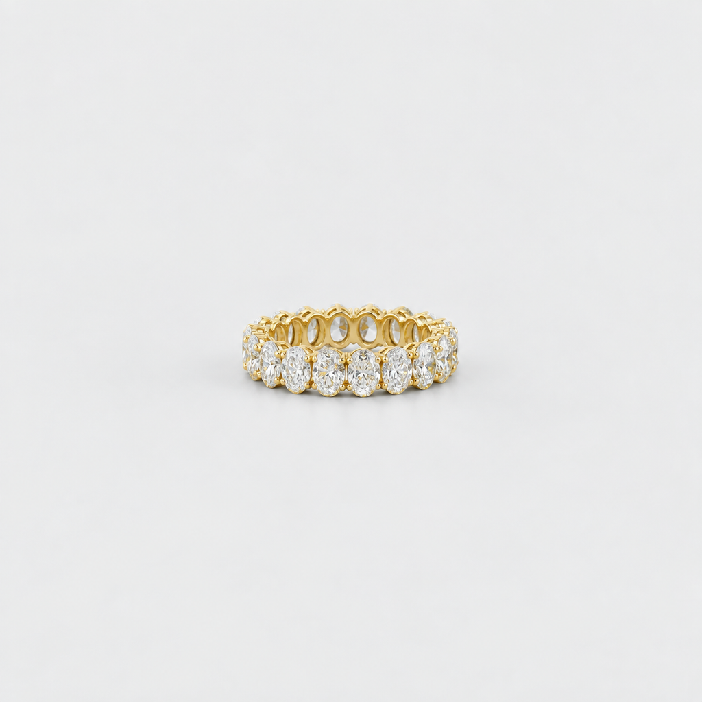A yellow gold eternity ring set with round brilliant-cut diamonds, photographed on a clean, light gray background.