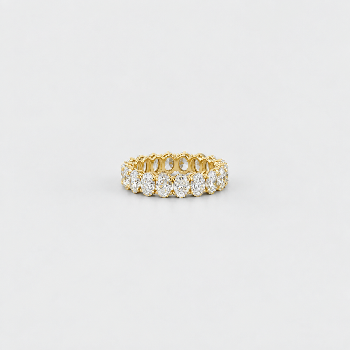 A yellow gold eternity ring set with round brilliant-cut diamonds, photographed on a clean, light gray background.