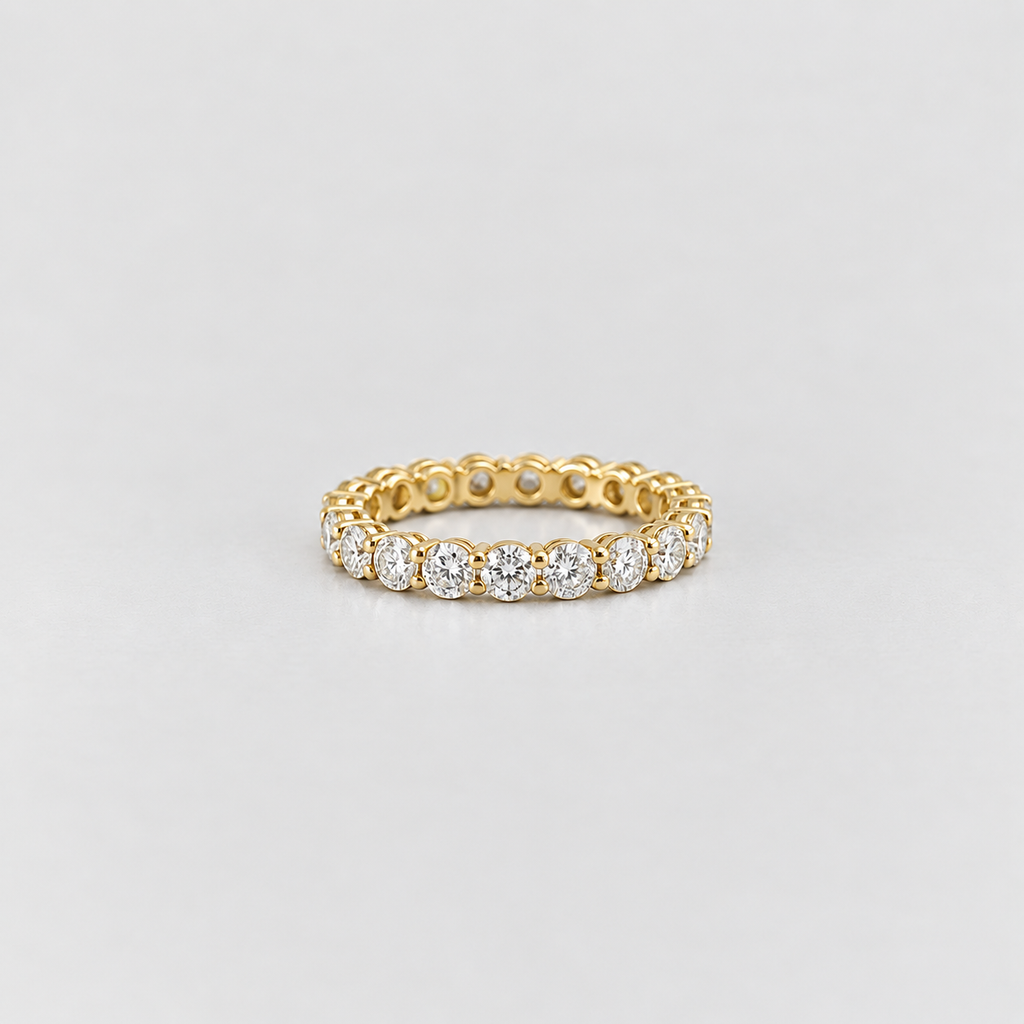 A yellow gold eternity ring featuring a continuous row of round-cut clear gemstones, photographed on a clean light gray background.