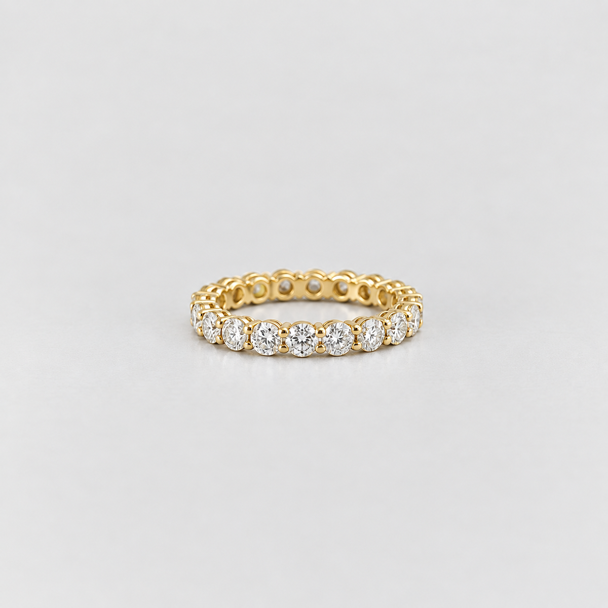 A yellow gold eternity ring featuring a continuous row of round-cut clear gemstones, photographed on a clean light gray background.